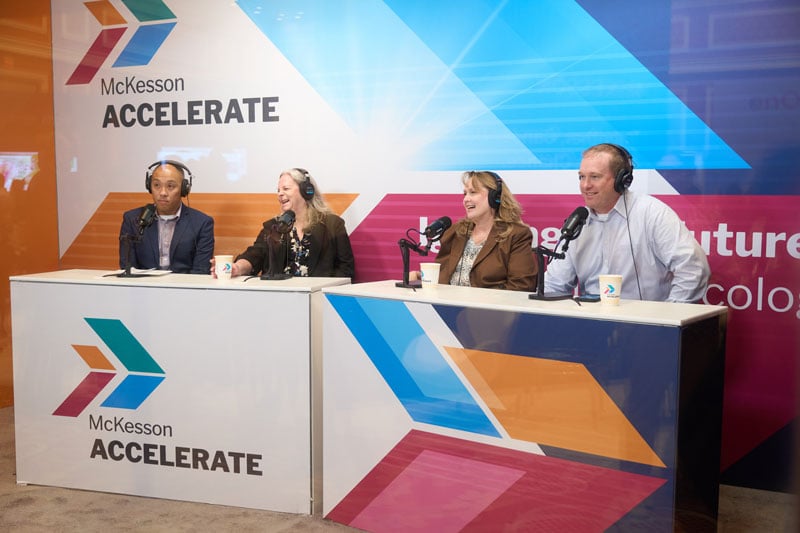 Four panelists wearing headsets sit behind a desk with microphones at a McKesson Accelerate broadcast, speaking during a live discussion.
