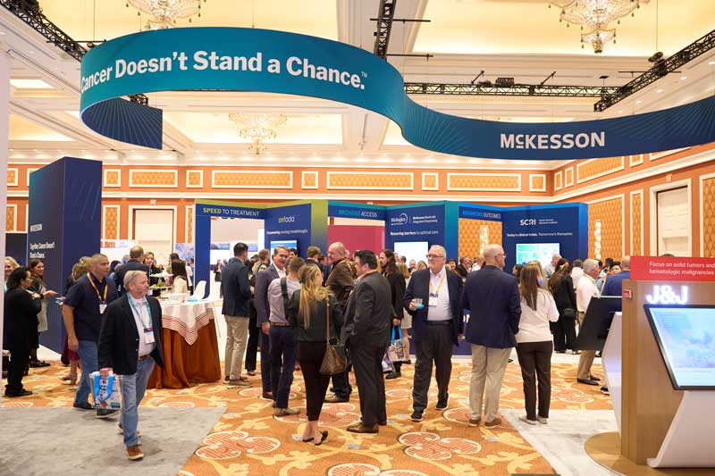 Crowd of professionals networking at a McKesson trade show booth under a large banner reading “Cancer Doesn’t Stand a Chance” in a hotel ballroom.